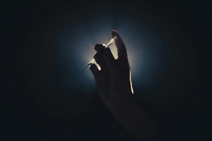 A silhouetted hand holds a syringe for hair botox treatment