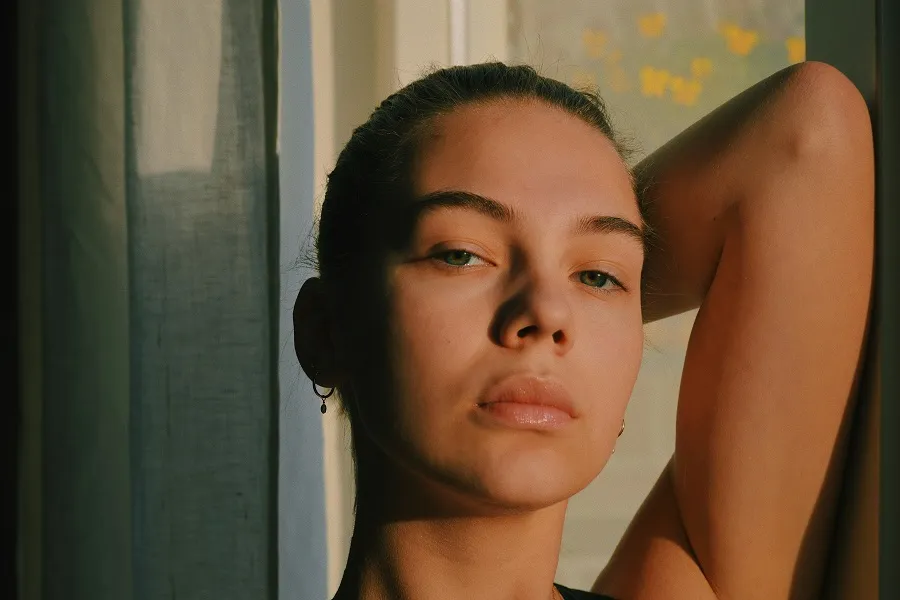 A silhouette of a person with one arm raised, leaning against a window with soft natural light illuminating the scene